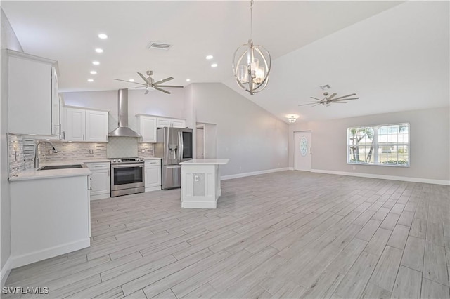 kitchen with ceiling fan with notable chandelier, appliances with stainless steel finishes, wall chimney range hood, and a sink