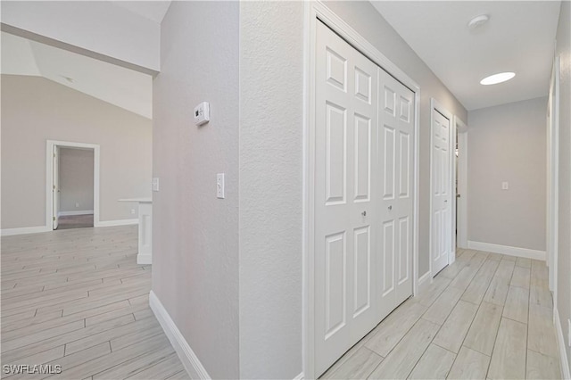 corridor with wood finish floors, baseboards, and lofted ceiling