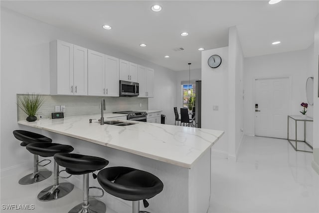 kitchen with a breakfast bar area, light stone countertops, a sink, stainless steel appliances, and tasteful backsplash