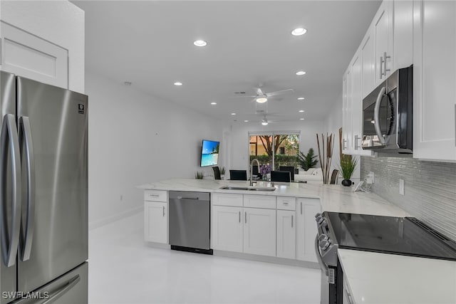 kitchen with backsplash, a peninsula, white cabinets, stainless steel appliances, and a sink