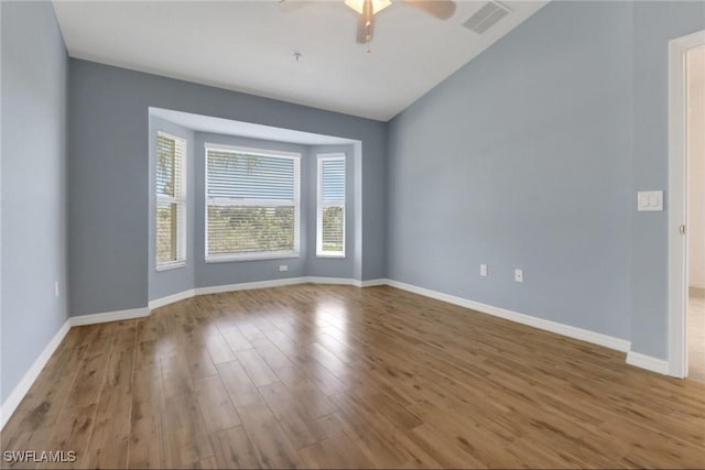 spare room with a ceiling fan, wood finished floors, visible vents, baseboards, and vaulted ceiling