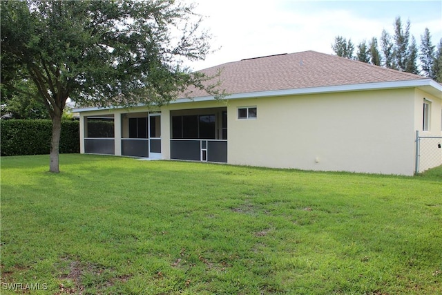 rear view of property with roof with shingles, a lawn, a sunroom, and stucco siding