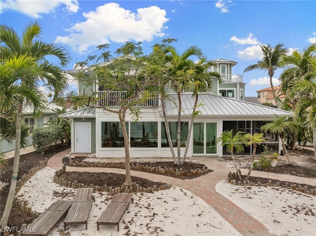 back of property featuring a balcony, a standing seam roof, a sunroom, decorative driveway, and metal roof