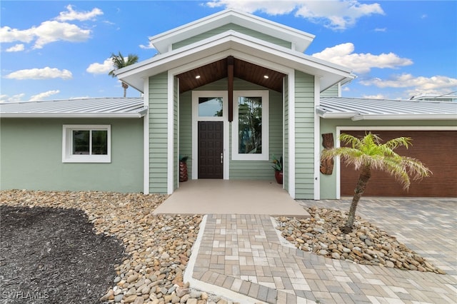 doorway to property featuring a garage, metal roof, decorative driveway, and a standing seam roof