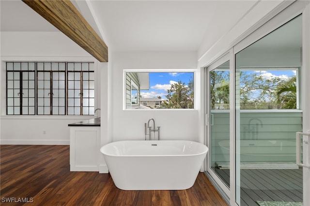 bathroom featuring beam ceiling, a freestanding tub, baseboards, and wood finished floors