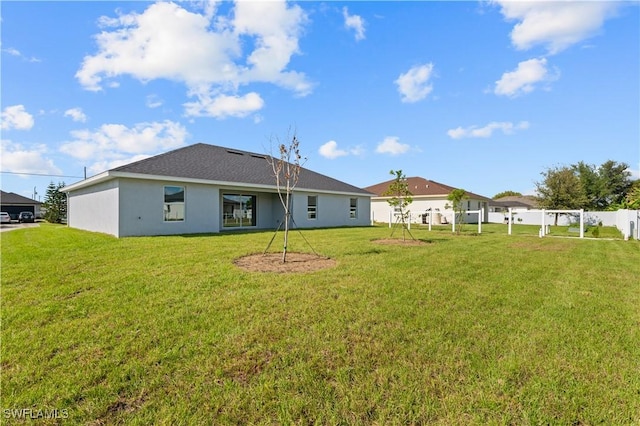 back of house featuring stucco siding, a yard, and fence