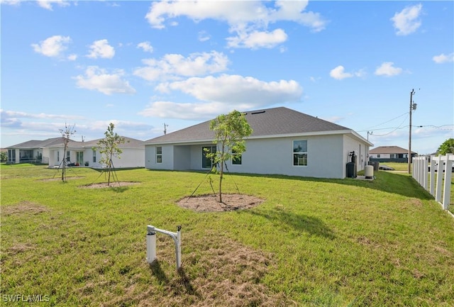 rear view of property featuring stucco siding, a lawn, and fence