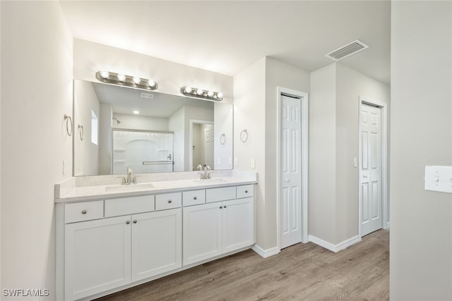 full bathroom featuring wood finished floors, baseboards, visible vents, double vanity, and a sink