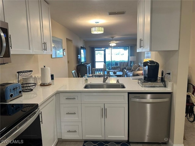 kitchen with a peninsula, stainless steel appliances, white cabinetry, a ceiling fan, and a sink