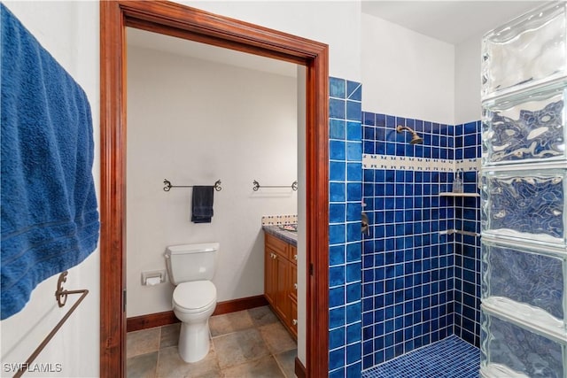 bathroom with vanity, toilet, baseboards, and a tile shower