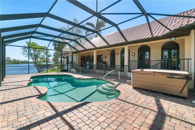 pool with a patio, a water view, a lanai, and a hot tub