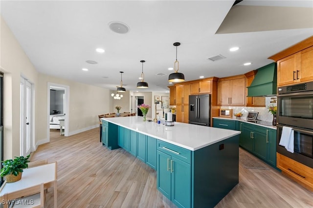 kitchen featuring visible vents, custom exhaust hood, a large island, high end black refrigerator, and multiple ovens