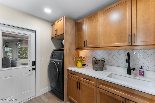 laundry area with baseboards, light wood-style flooring, washer / clothes dryer, cabinet space, and a sink