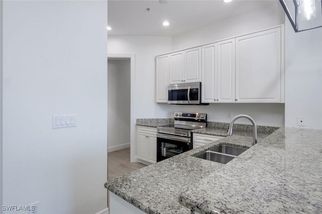 kitchen with a sink, light stone countertops, appliances with stainless steel finishes, and white cabinets