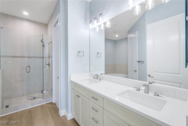 full bath with double vanity, wood finished floors, a stall shower, and a sink