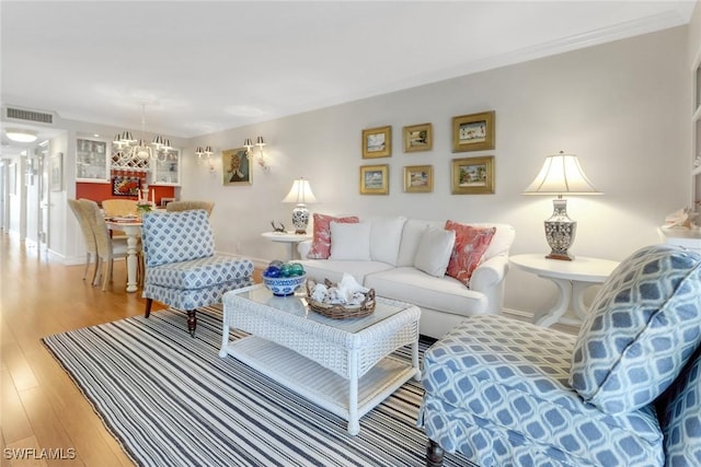 living area featuring light wood finished floors, visible vents, baseboards, ornamental molding, and a notable chandelier