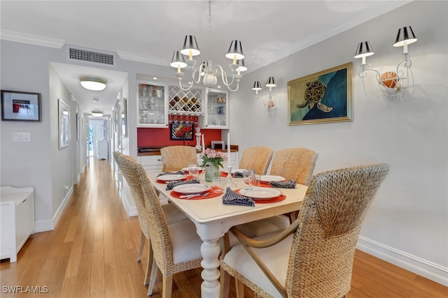 dining area with a notable chandelier, visible vents, crown molding, and light wood-style floors