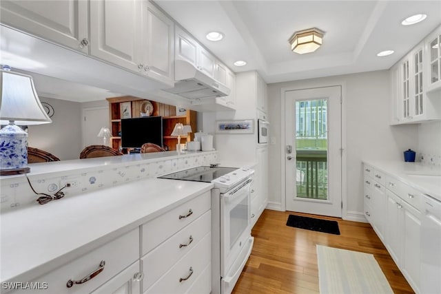 kitchen with glass insert cabinets, light wood-style flooring, white appliances, and a raised ceiling