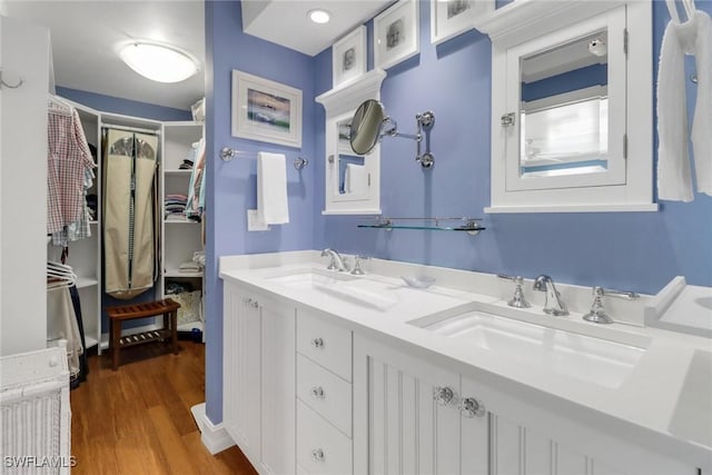 bathroom with double vanity, wood finished floors, a walk in closet, and a sink