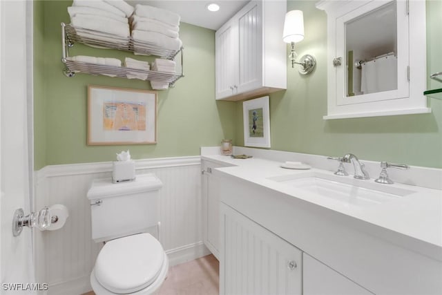 bathroom featuring vanity, toilet, and a wainscoted wall