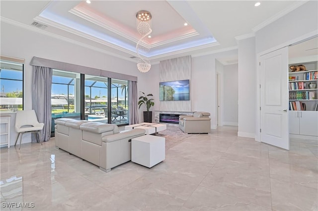 living area with visible vents, a tray ceiling, a glass covered fireplace, a high ceiling, and crown molding