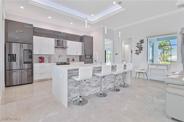 kitchen with a kitchen bar, modern cabinets, stainless steel appliances, wall chimney exhaust hood, and light countertops