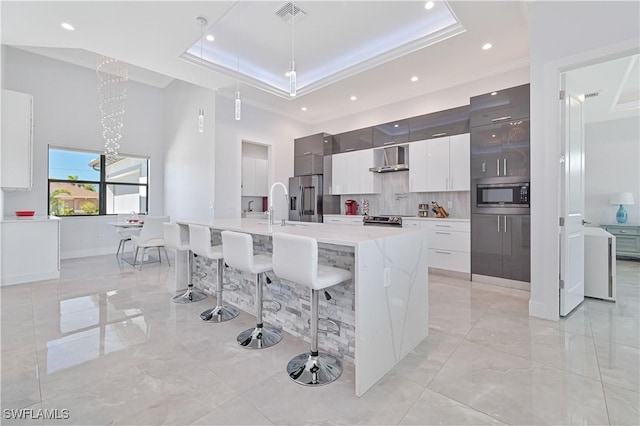 kitchen featuring visible vents, appliances with stainless steel finishes, a raised ceiling, modern cabinets, and wall chimney exhaust hood