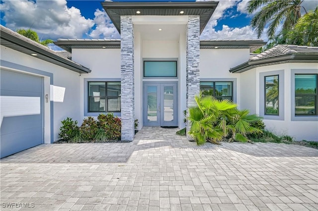 view of exterior entry with a tiled roof, stucco siding, french doors, and driveway