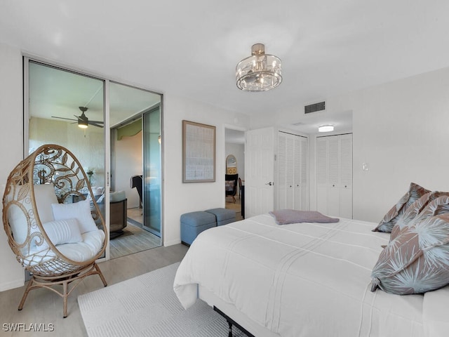 bedroom featuring visible vents, multiple closets, a notable chandelier, wood finished floors, and baseboards