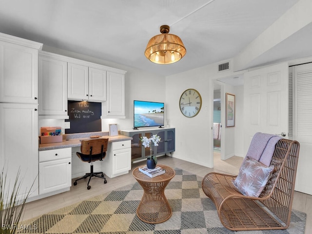 home office with visible vents, light wood-style flooring, baseboards, and built in desk