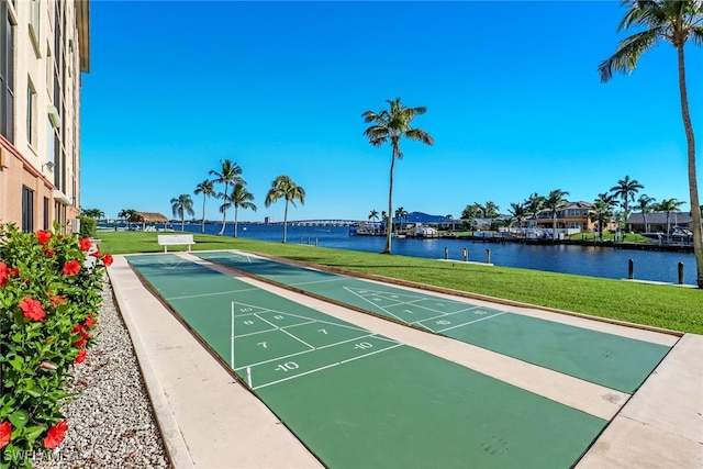 view of property's community with shuffleboard, a lawn, and a water view