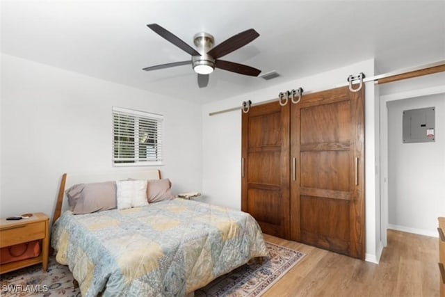 bedroom with electric panel, a barn door, light wood-style floors, and visible vents