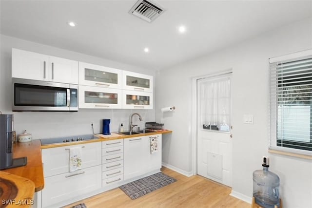 kitchen with stainless steel microwave, visible vents, black electric stovetop, white cabinets, and a sink