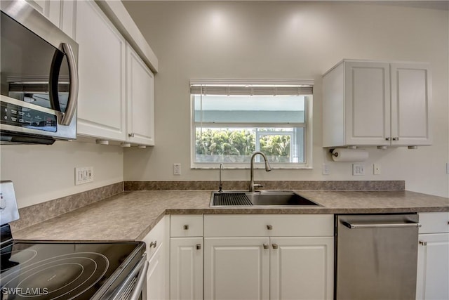 kitchen with dark countertops, white cabinets, appliances with stainless steel finishes, and a sink