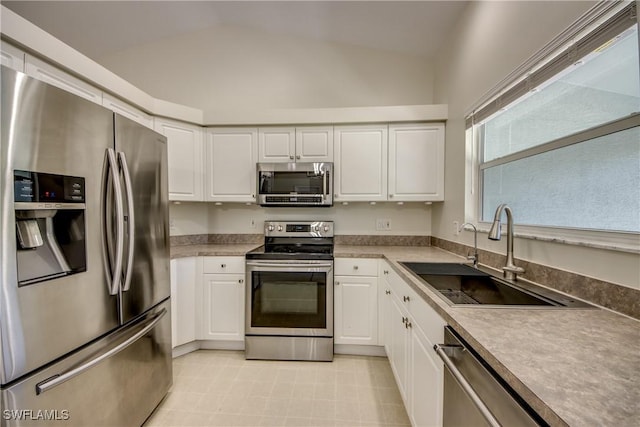 kitchen featuring vaulted ceiling, white cabinetry, stainless steel appliances, and a sink