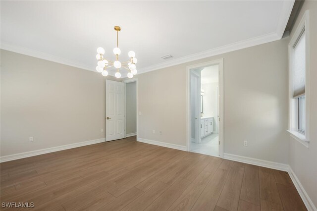 spare room with a notable chandelier, wood finished floors, baseboards, and ornamental molding