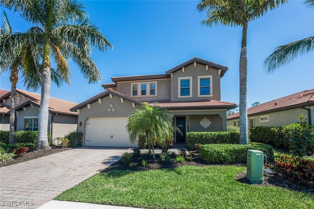 mediterranean / spanish home featuring a front yard, stucco siding, a garage, a tiled roof, and decorative driveway