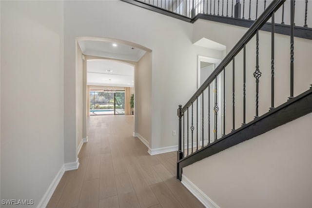 interior space featuring wood finished floors, arched walkways, baseboards, a towering ceiling, and stairs