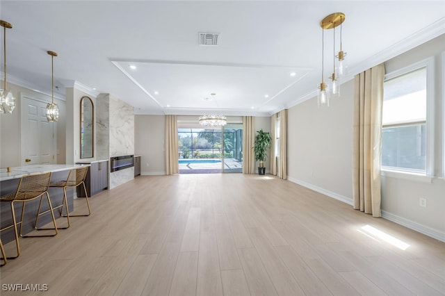 living area featuring light wood finished floors, baseboards, crown molding, and an inviting chandelier