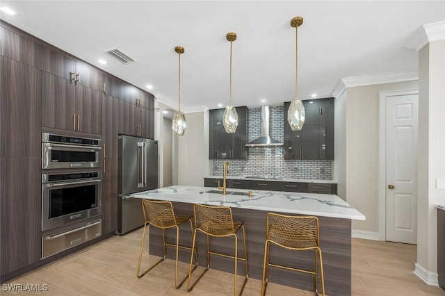 kitchen featuring a warming drawer, visible vents, a sink, appliances with stainless steel finishes, and wall chimney range hood