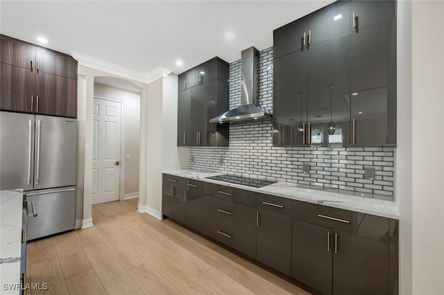 kitchen featuring black electric stovetop, wall chimney range hood, light wood-type flooring, decorative backsplash, and high quality fridge
