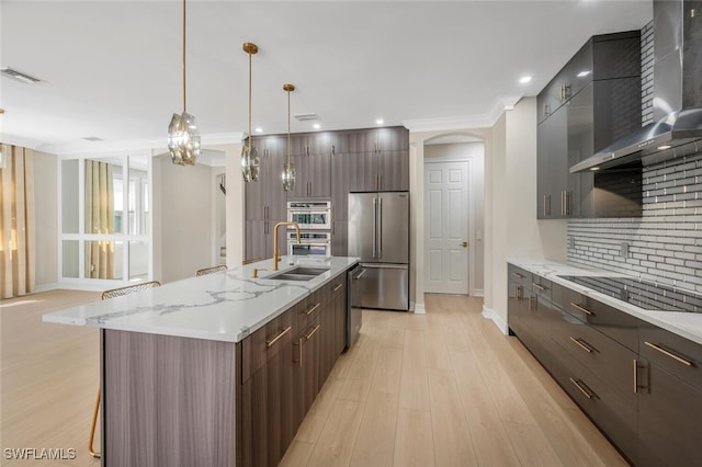 kitchen featuring visible vents, a sink, stainless steel appliances, wall chimney exhaust hood, and modern cabinets