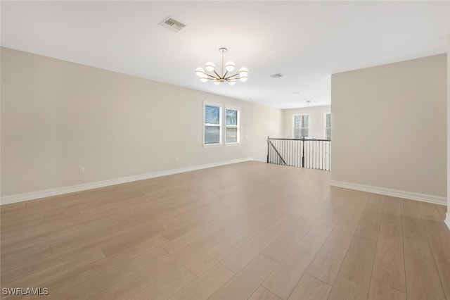 unfurnished room with visible vents, baseboards, an inviting chandelier, and light wood-style flooring