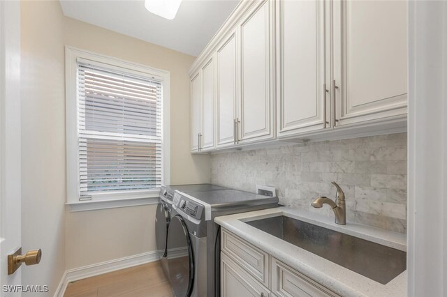 washroom featuring independent washer and dryer, a sink, cabinet space, light wood-style floors, and baseboards