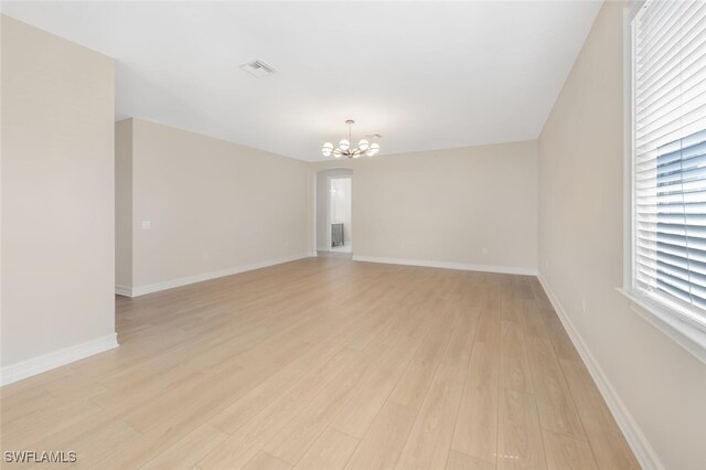 spare room with a notable chandelier, baseboards, light wood-type flooring, and visible vents