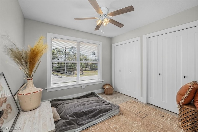 bedroom with ceiling fan, baseboards, multiple closets, and wood finished floors