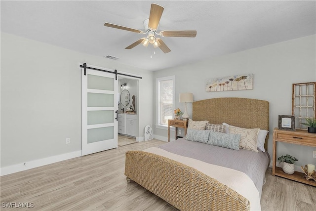 bedroom with visible vents, a barn door, connected bathroom, light wood finished floors, and baseboards