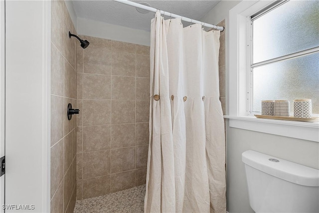 bathroom featuring a textured ceiling, toilet, and a tile shower