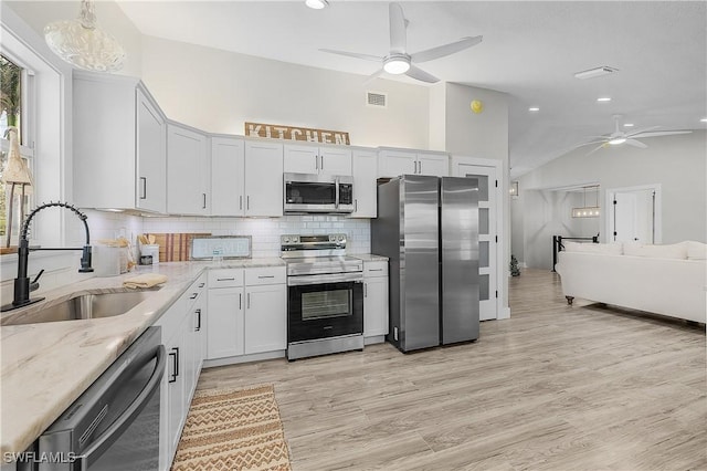 kitchen with light stone counters, a ceiling fan, a sink, stainless steel appliances, and backsplash