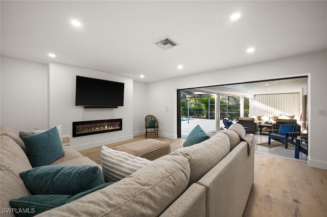 living area with visible vents, baseboards, light wood-style flooring, recessed lighting, and a glass covered fireplace